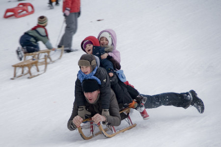 A man carries three children on his back as he sleds down a slop